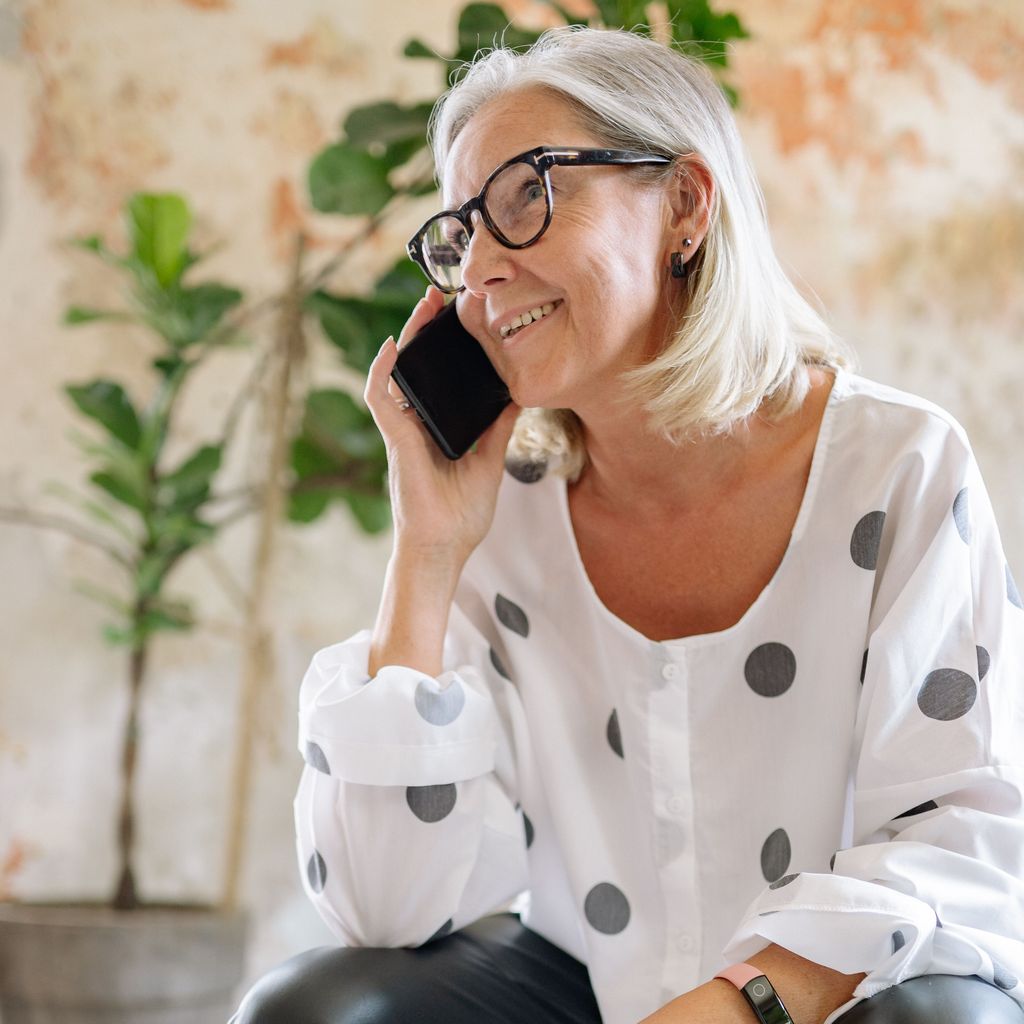 An older woman smiling as she talks on the phone at home in daylight.
